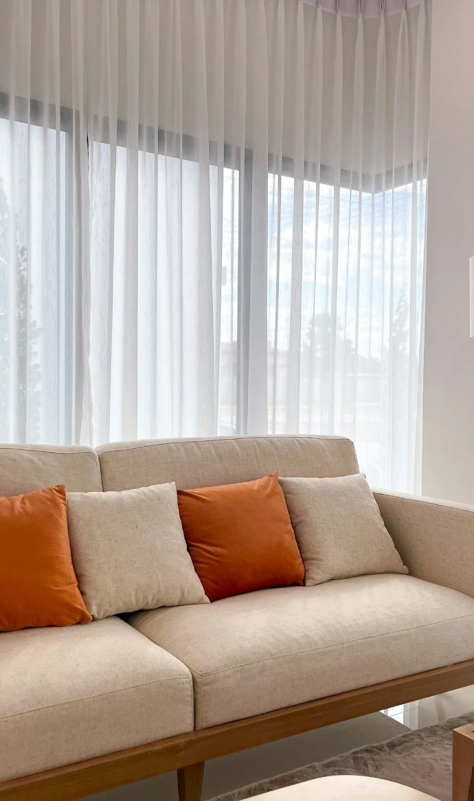 A couch with orange pillows sits by a window